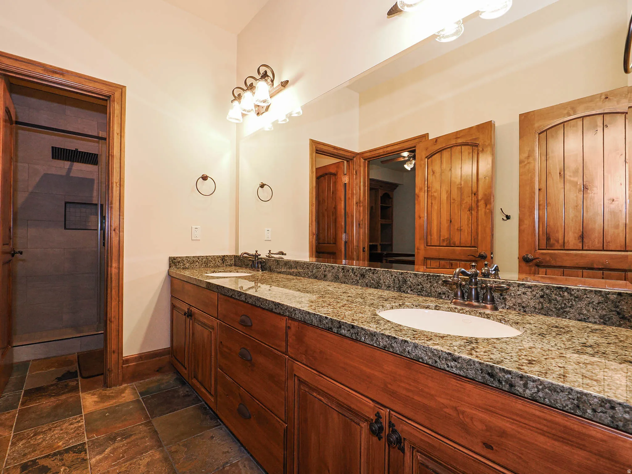 Full bath featuring double vanity, a stall shower, and stone tile flooring