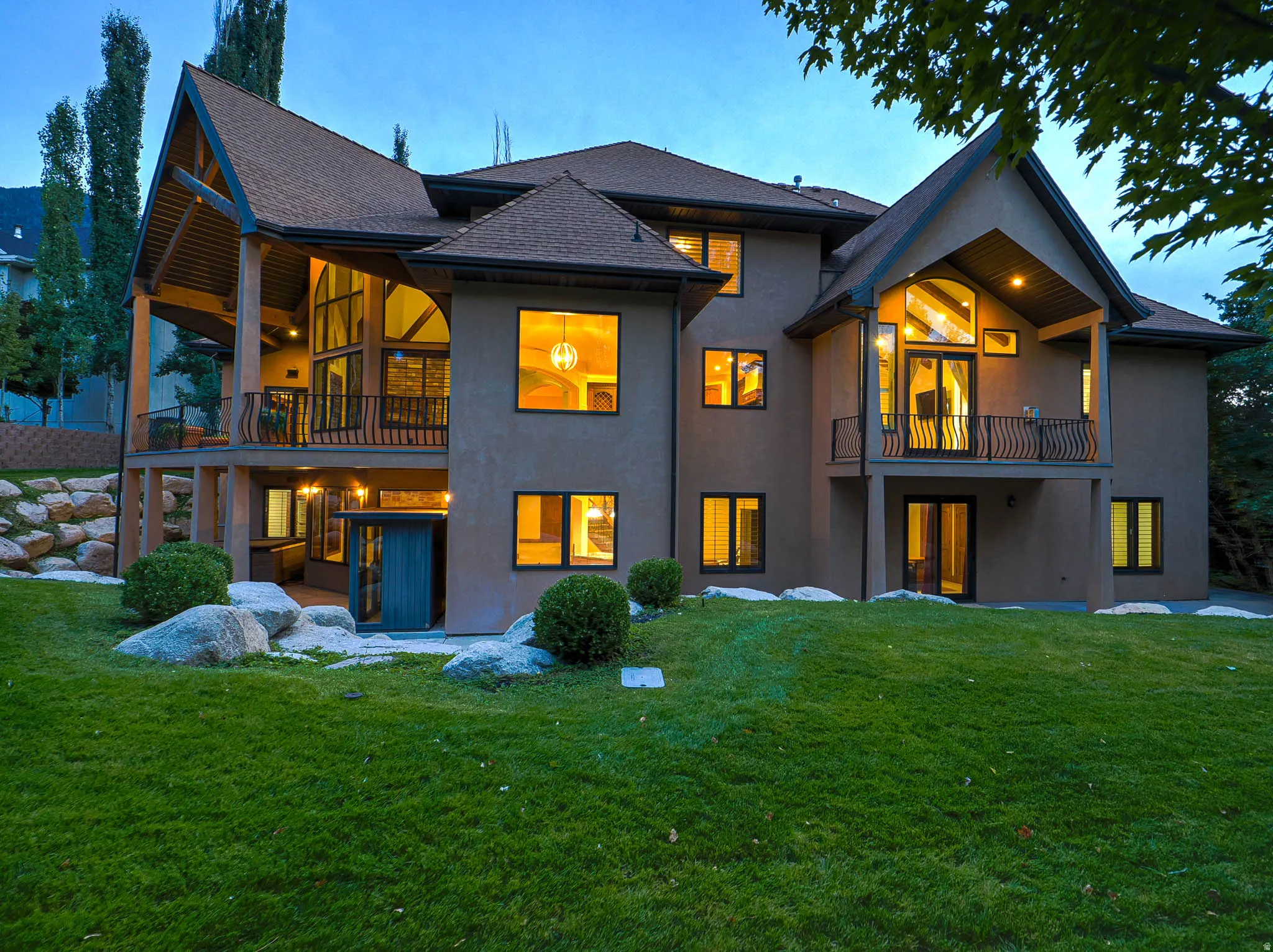 Back of house featuring a balcony, a lawn, a patio area, stucco siding, and a shingled roof