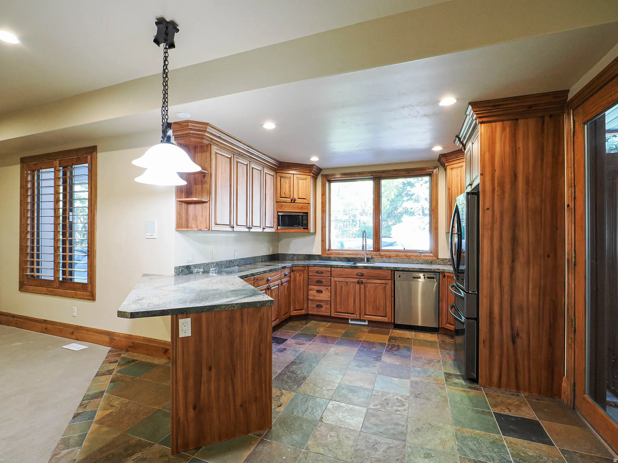 Kitchen featuring stone tile floors, wood finish cabinetry, stainless steel appliances, and a peninsula