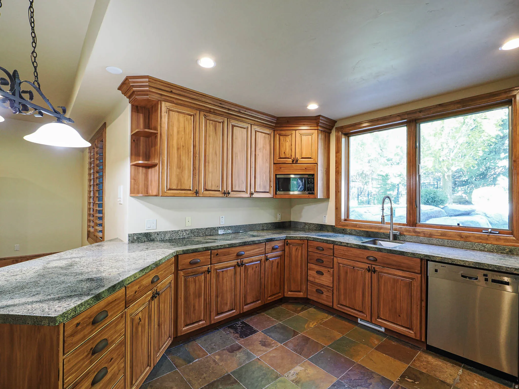 Kitchen featuring wood finish cabinetry, stainless steel appliances, a peninsula, dark stone finish floors, and open shelves