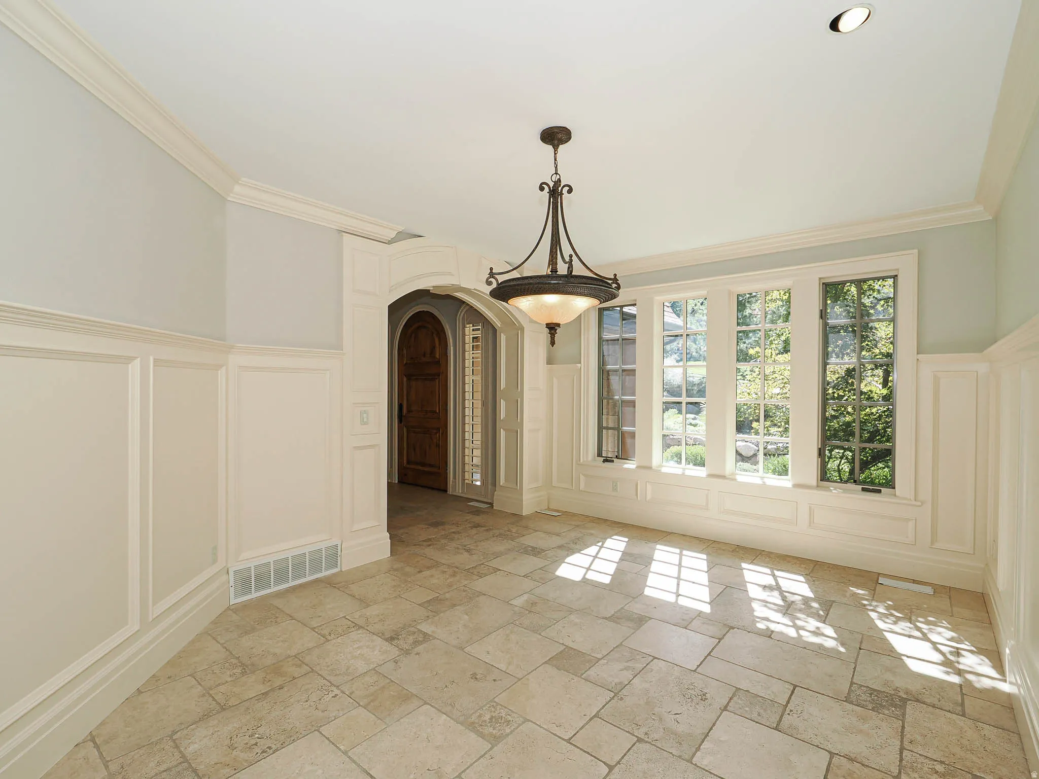 Unfurnished dining area with a decorative wall, arched walkways, wainscoting, stone tile flooring, and ornamental molding