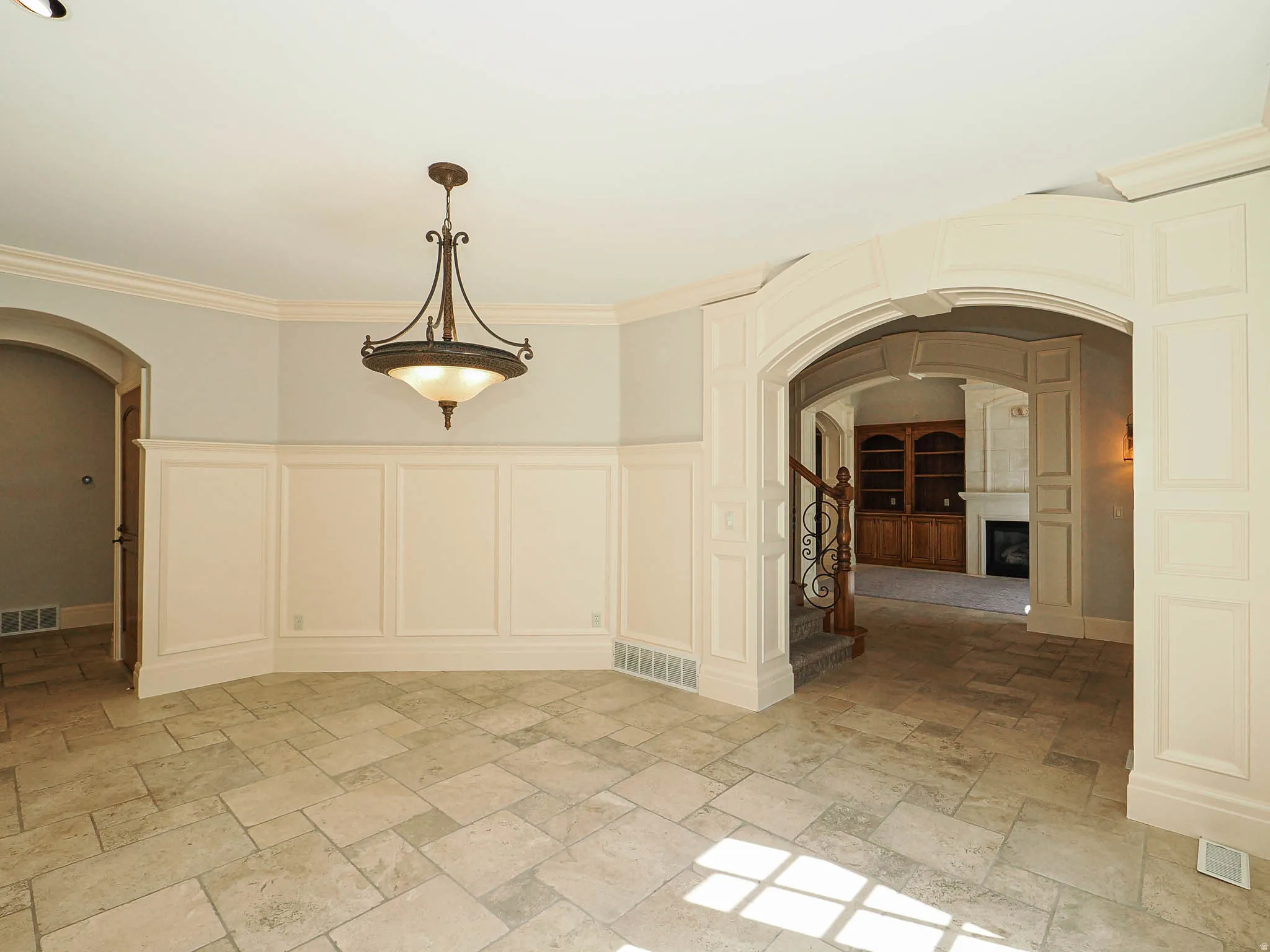 Spare room with arched walkways, a decorative wall, a wainscoted wall, stone tile floors, and crown molding