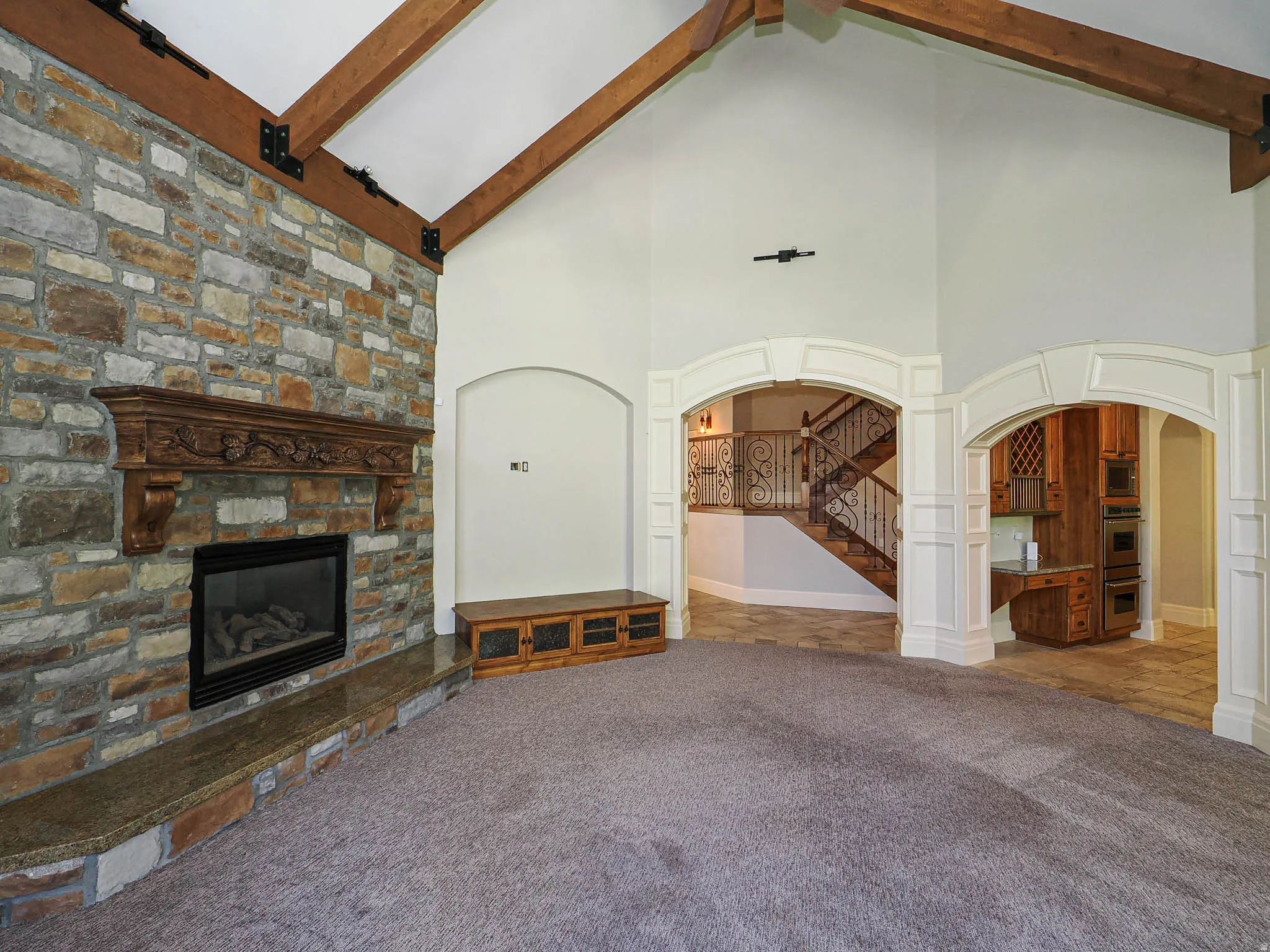 Unfurnished living room with arched walkways, carpet, and a stone fireplace