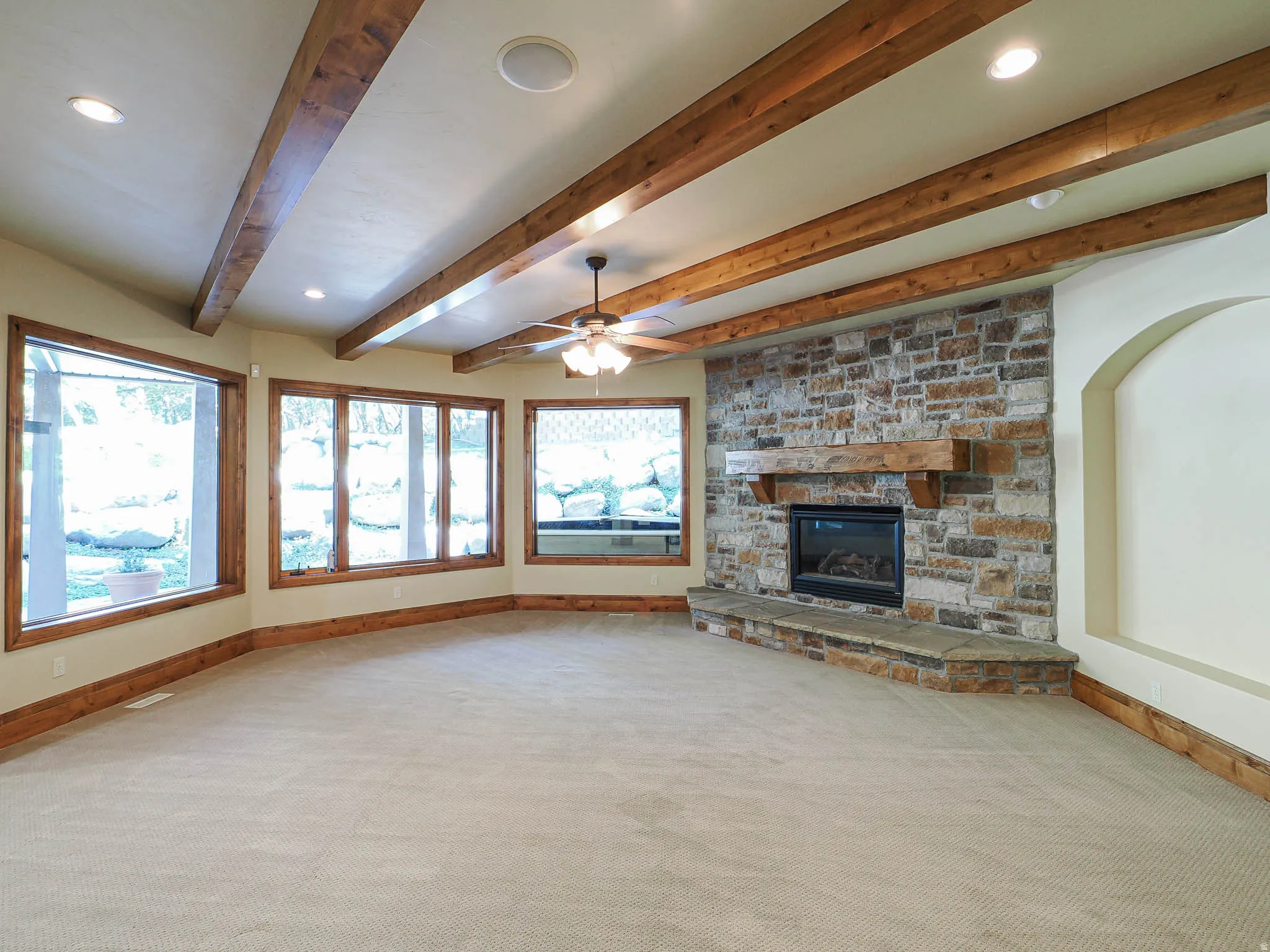 Unfurnished living room featuring recessed lighting, a stone fireplace, beamed ceiling, ceiling fan, and light carpet