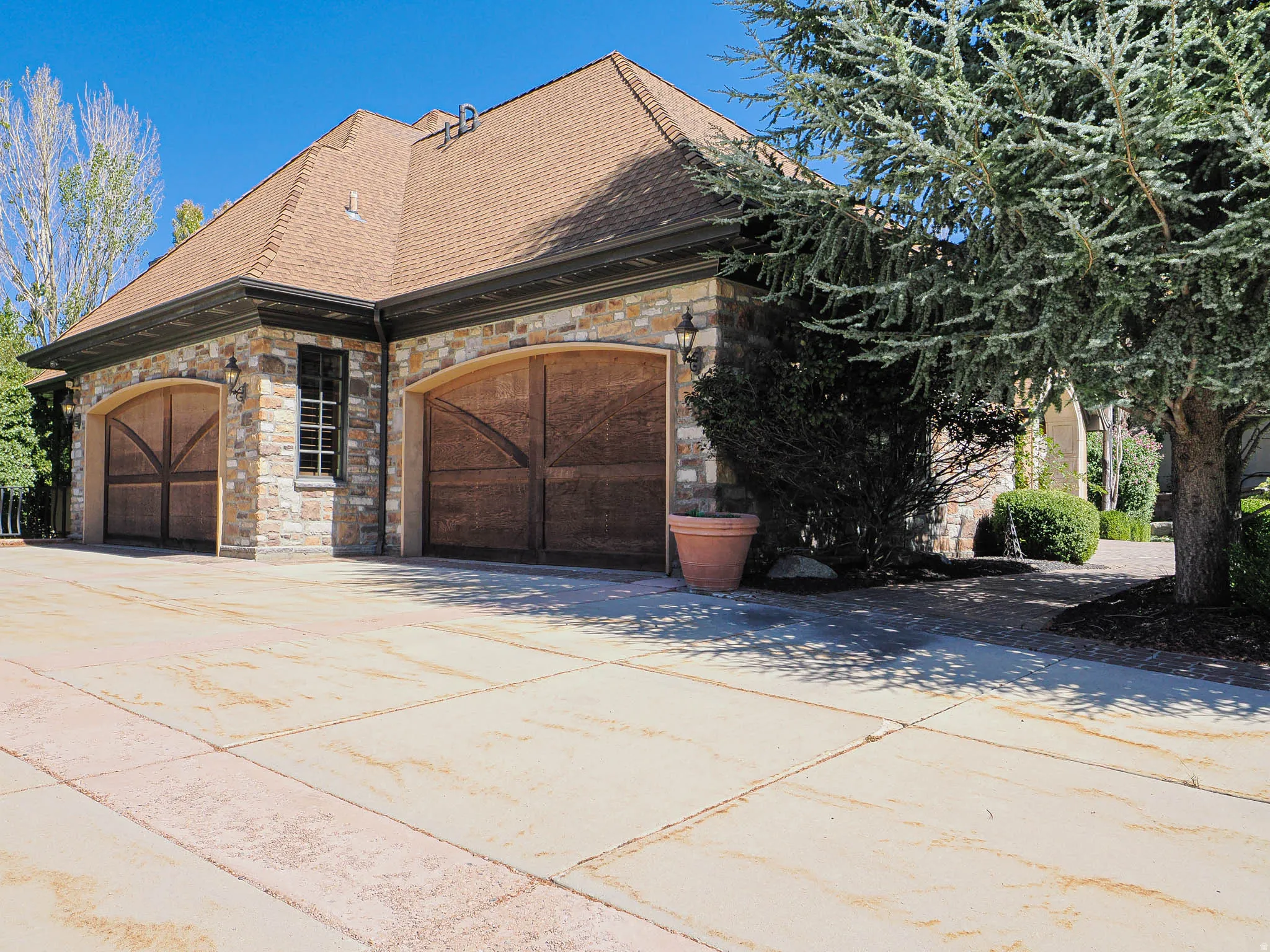 View of side of home with stone siding, concrete driveway, a shingled roof, and an attached garage