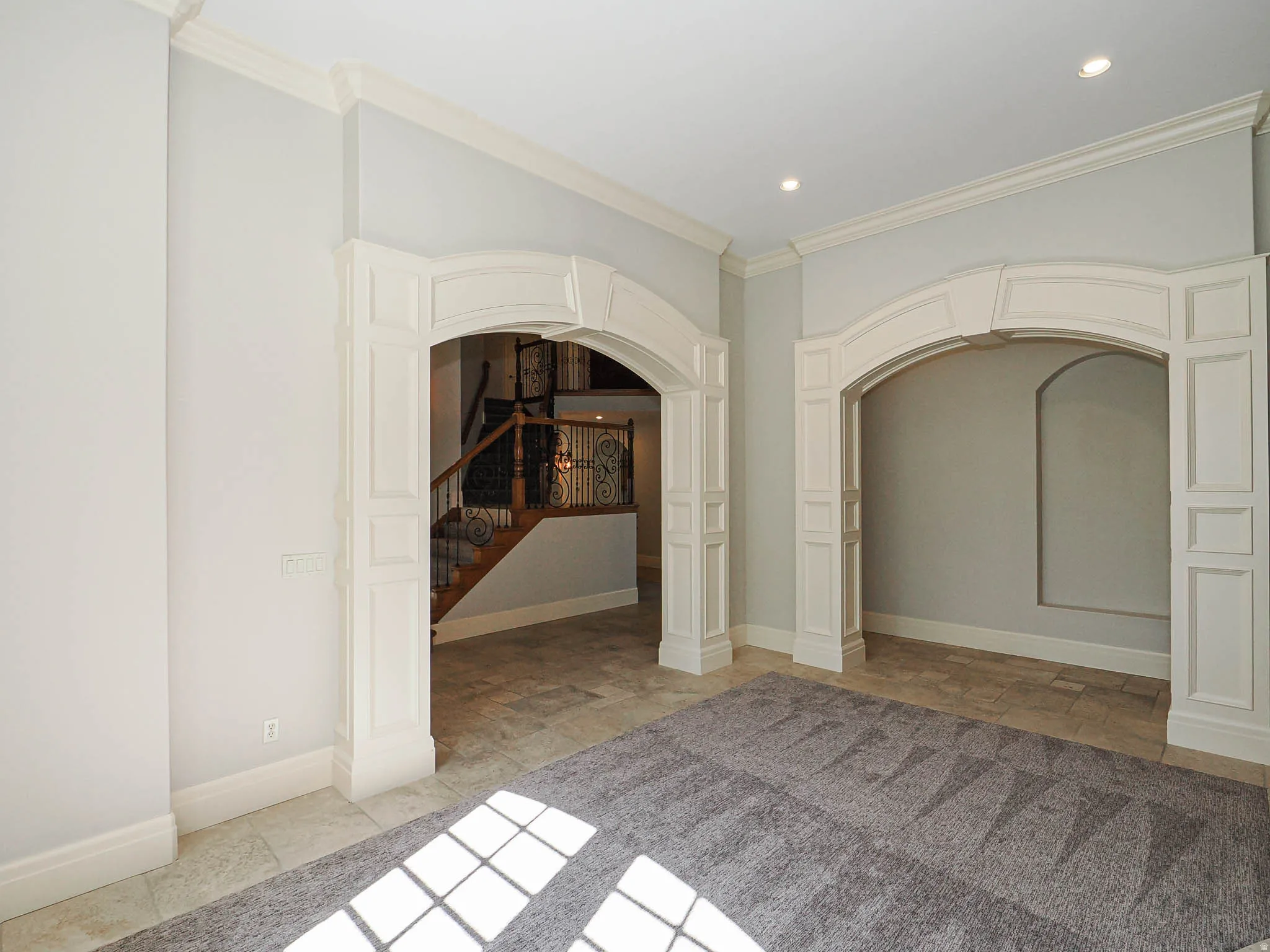 Empty room with arched walkways, stone tile flooring, and crown molding