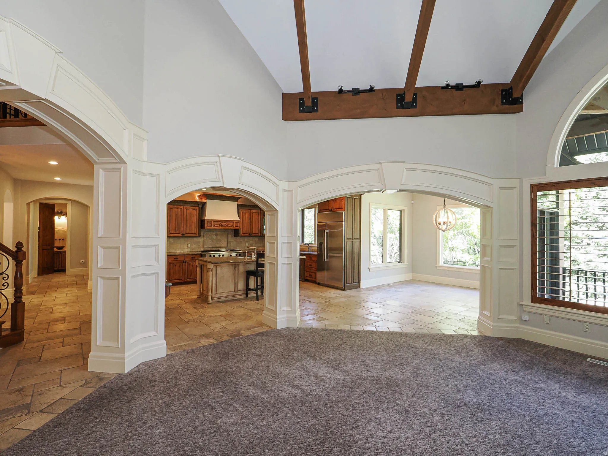 Unfurnished living room featuring arched walkways, stone tile floors, healthy amount of natural light, and vaulted ceiling