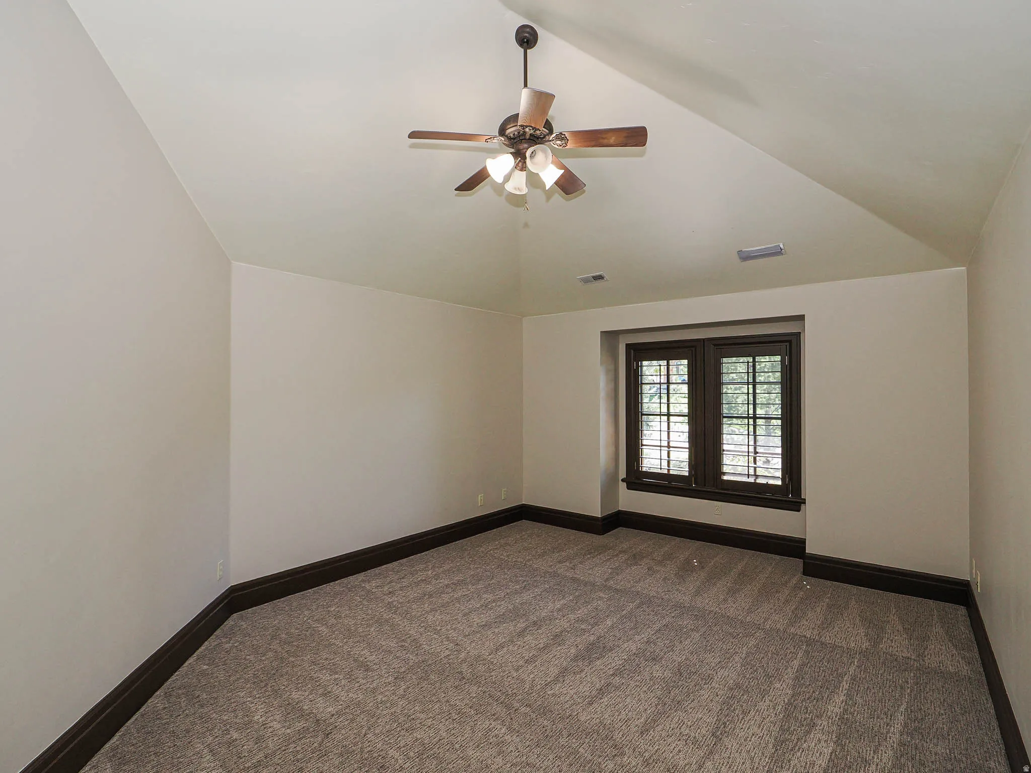 Unfurnished room featuring a ceiling fan, dark carpet, and lofted ceiling