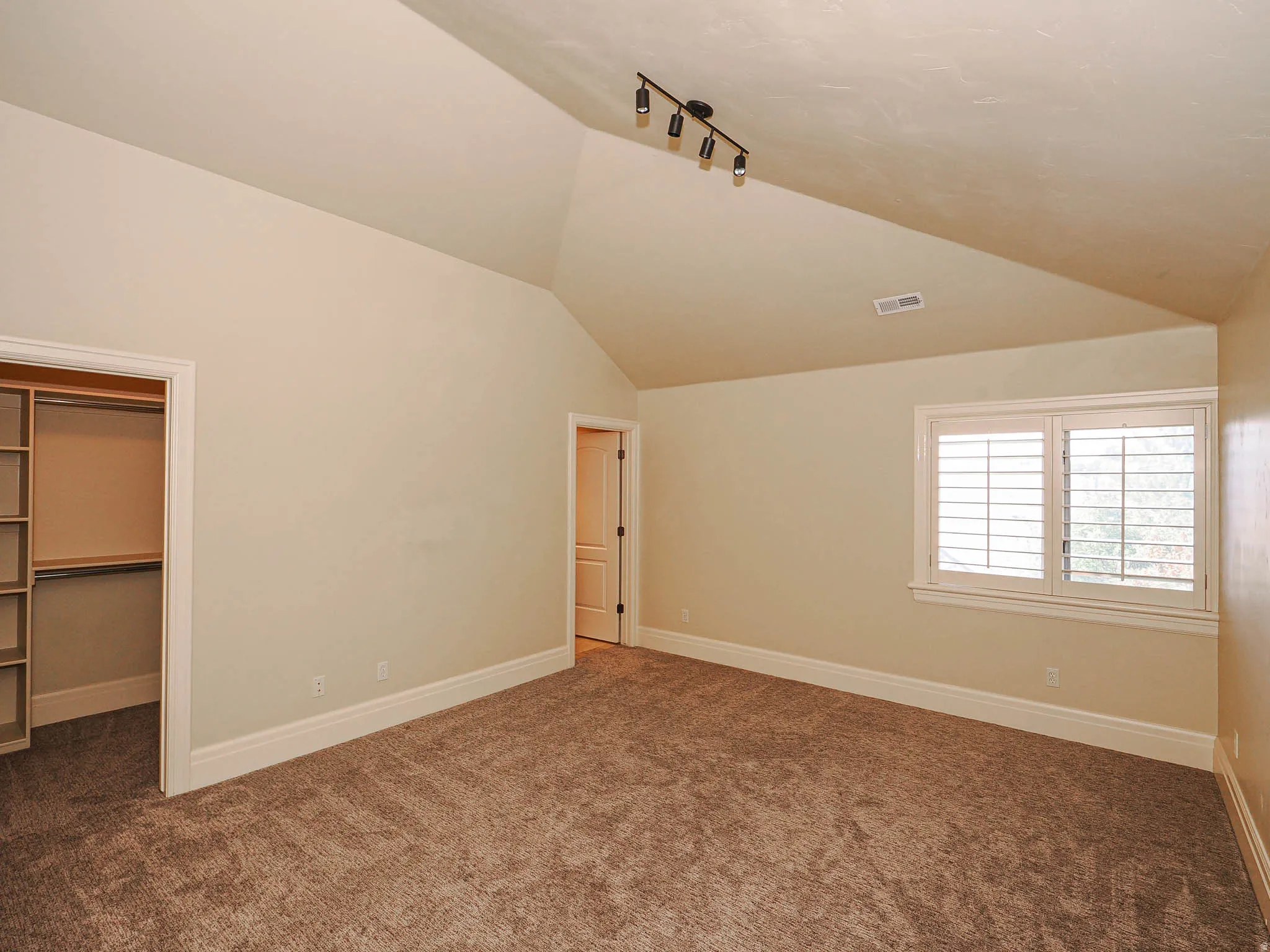 Unfurnished bedroom featuring rail lighting, a walk in closet, dark colored carpet, and vaulted ceiling