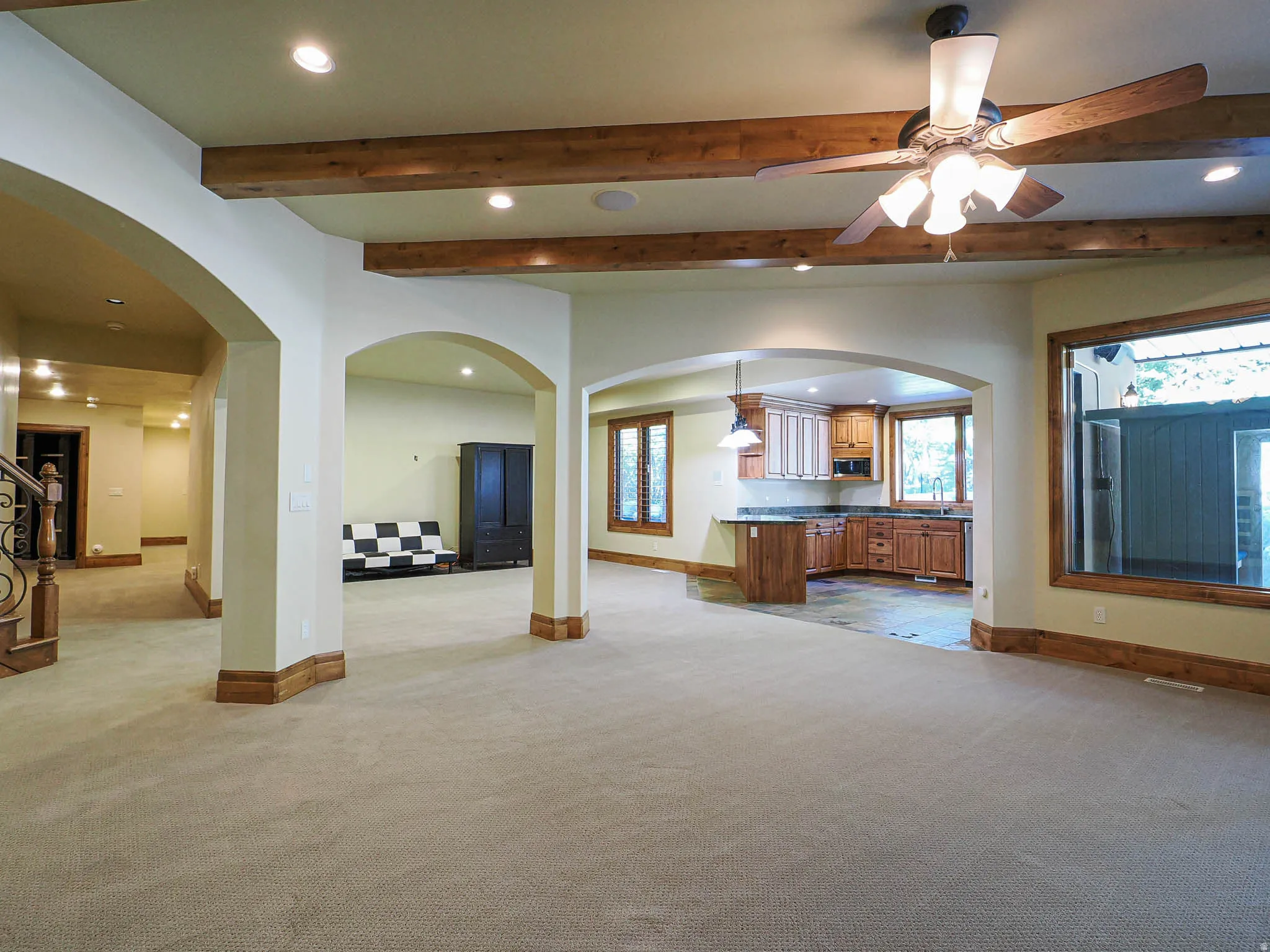 Unfurnished living room with arched walkways, recessed lighting, beamed ceiling, a ceiling fan, and light colored carpet