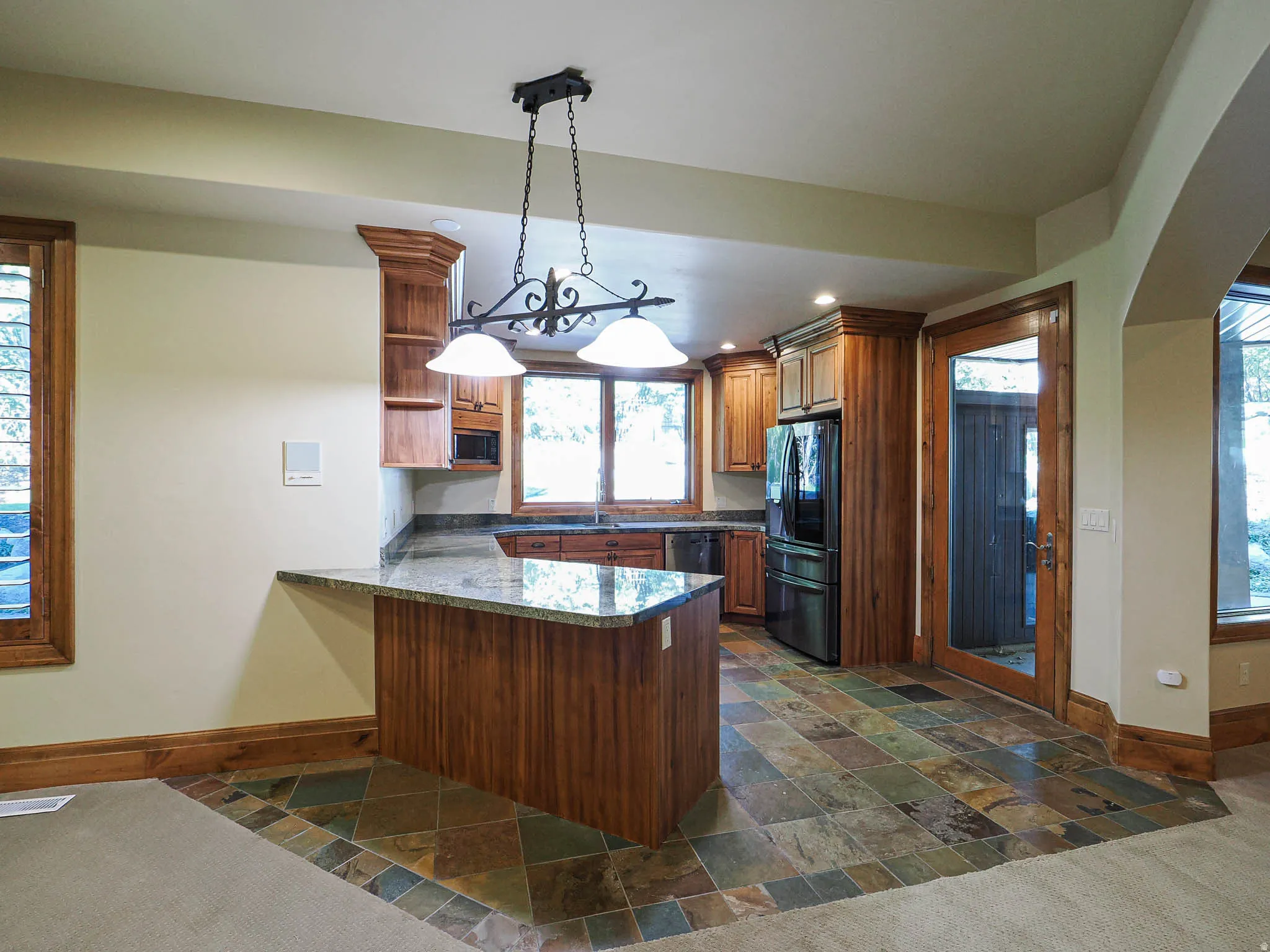 Kitchen with a peninsula, stone tile flooring, black refrigerator with ice dispenser, wood finish cabinetry, and dark stone counters
