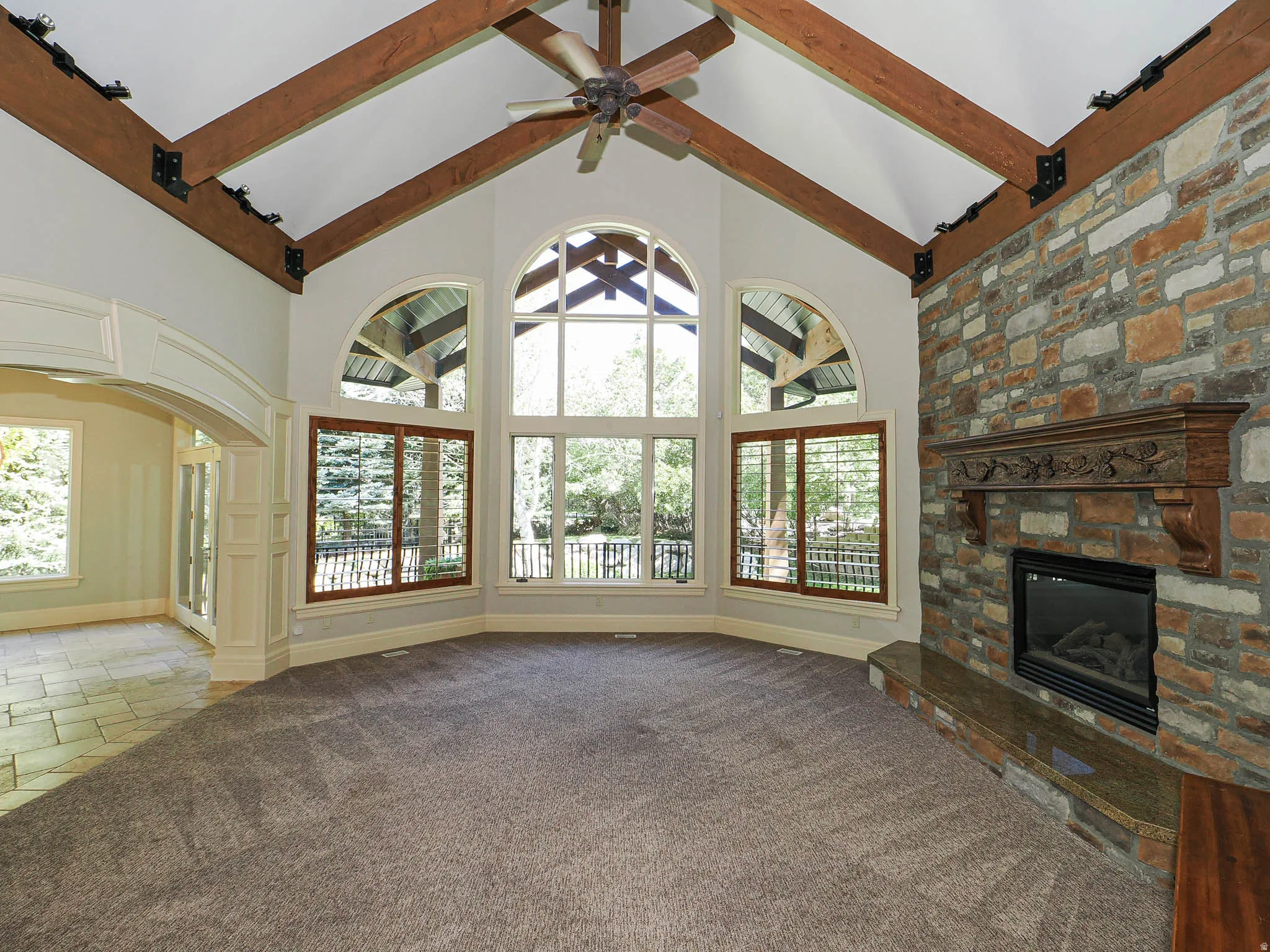 Unfurnished living room featuring a stone fireplace, carpet floors, stone tile floors, a ceiling fan, and plenty of natural light