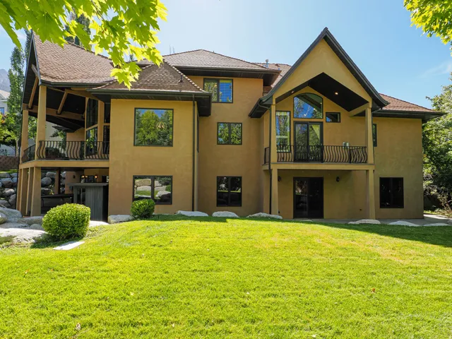 Back of property featuring a balcony, stucco siding, and a lawn