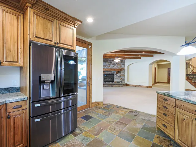 Kitchen with stainless steel fridge with ice dispenser, wood finish cabinetry, arched walkways, dark carpet, and stone tile floors