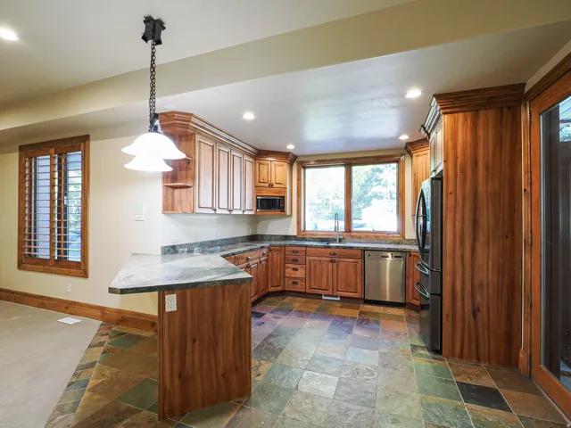 Kitchen featuring stone tile floors, wood finish cabinetry, stainless steel appliances, and a peninsula