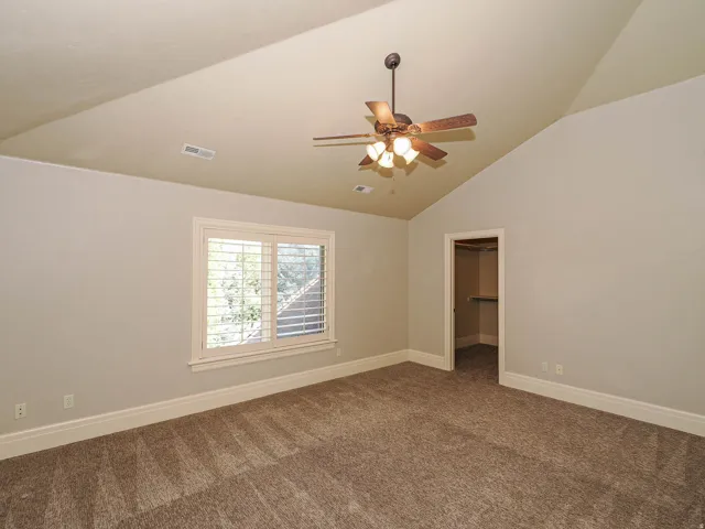 Spare room featuring dark colored carpet, ceiling fan, and vaulted ceiling