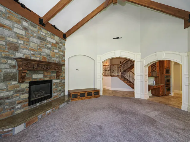 Unfurnished living room with arched walkways, carpet, and a stone fireplace
