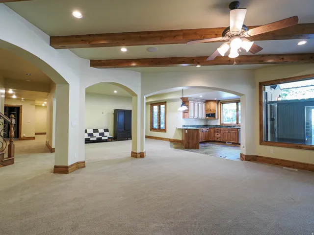 Unfurnished living room with arched walkways, recessed lighting, beamed ceiling, a ceiling fan, and light colored carpet