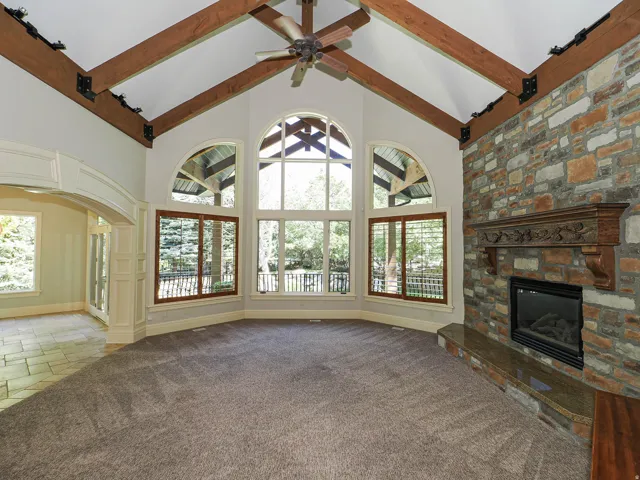 Unfurnished living room featuring a stone fireplace, carpet floors, stone tile floors, a ceiling fan, and plenty of natural light
