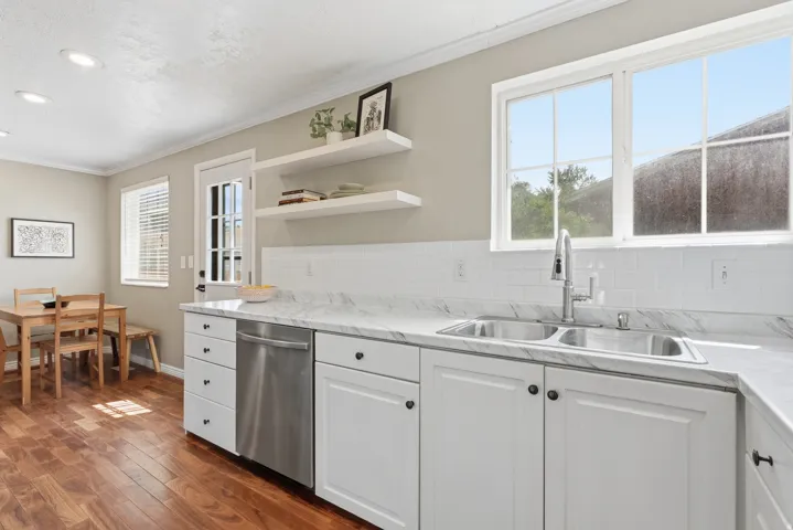 Kitchen featuring white shaker-style cabinetry, stainless steel dishwasher, dual basin sink with gooseneck faucet, white subway tile backsplash, and wood-finish flooring