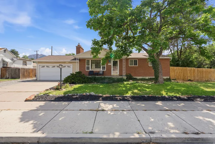 Brick exterior with white trim, featuring a front lawn with mature trees and a concrete driveway