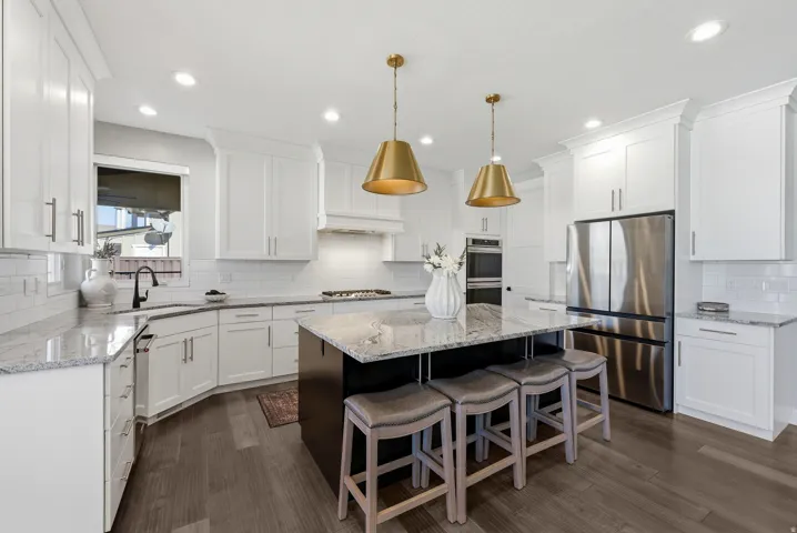 Kitchen featuring a dark wood-finish island with seating, white shaker-style cabinetry, stainless steel appliances, granite countertops, and two brass pendant lights