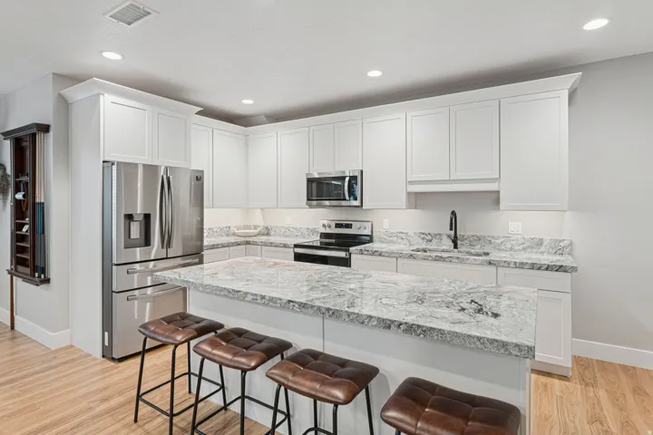 Kitchen with stainless steel appliances, light wood finished floors, a kitchen bar, light stone countertops, and white cabinets
