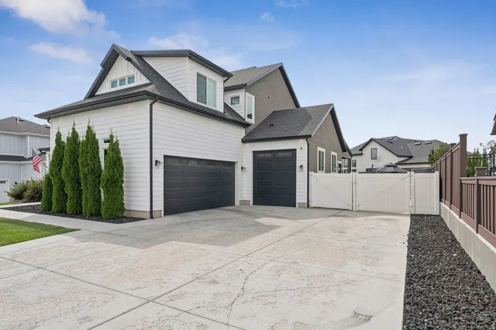 View of side of property featuring a gate, driveway, and roof with shingles