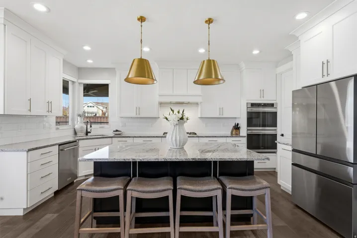 Open-concept kitchen featuring a large central island, white shaker cabinetry, stainless steel appliances, and wood-finish flooring