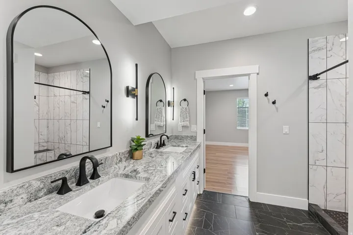 Bathroom with double vanity, a marble finish shower, dark marble finish flooring, and recessed lighting