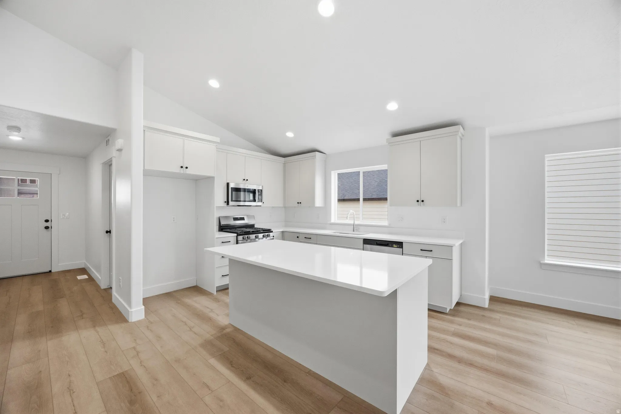 Kitchen featuring stainless steel appliances, a center island, light wood-style flooring, white cabinets, and lofted ceiling