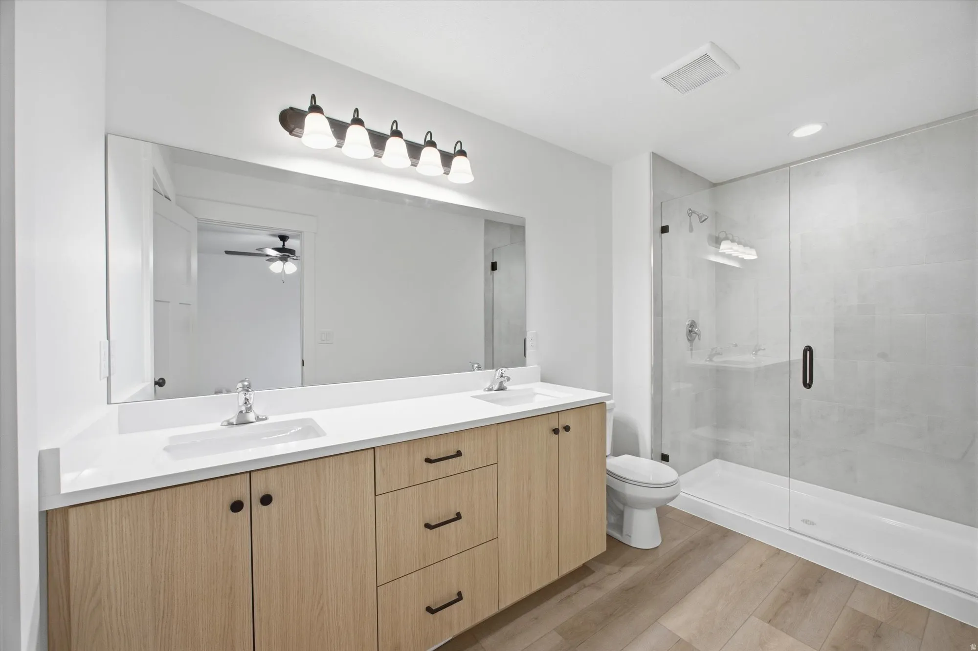 Full bath featuring double vanity, light wood finished floors, a stall shower, ceiling fan, and recessed lighting
