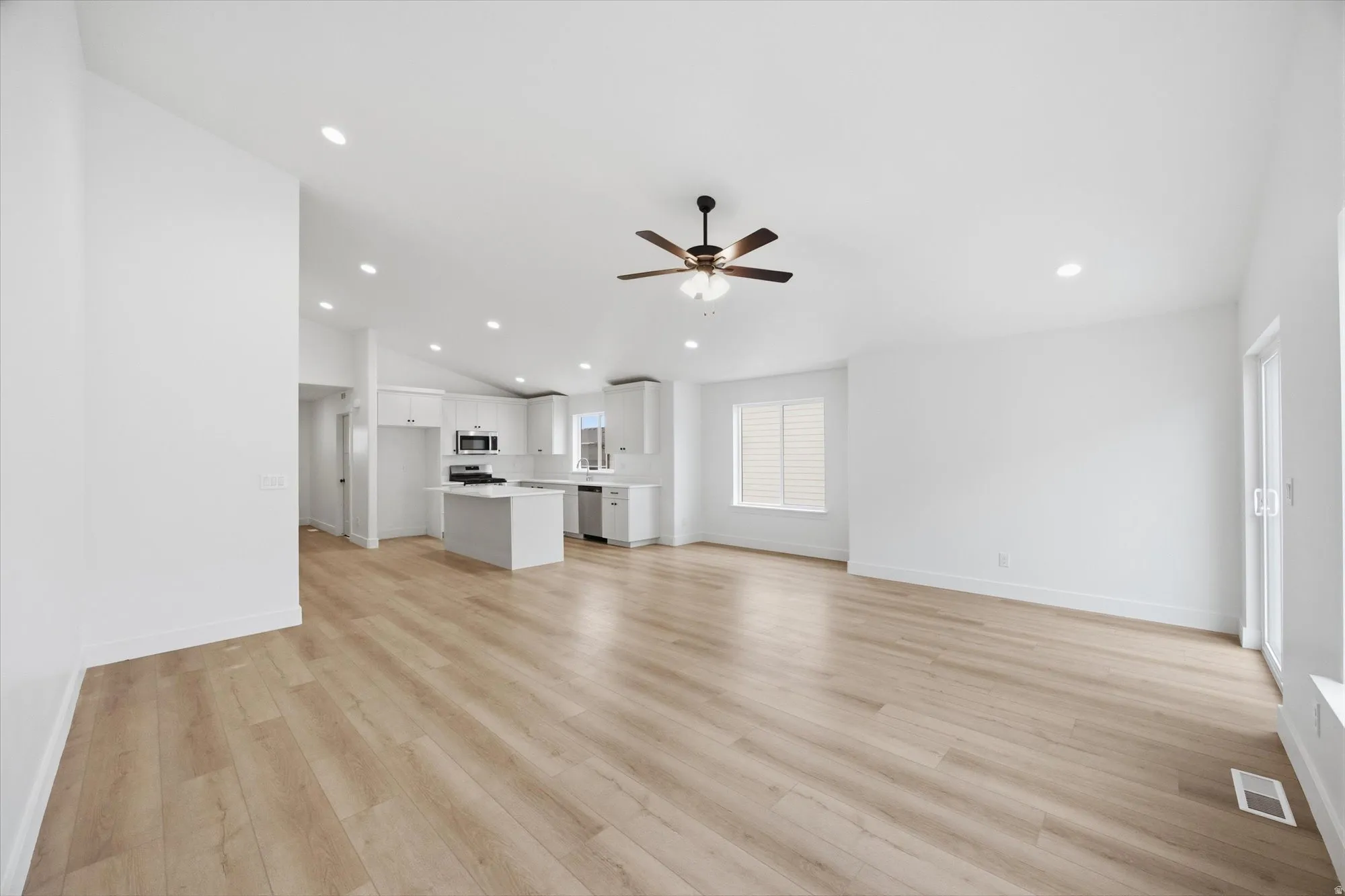 Unfurnished living room featuring light wood-style floors, ceiling fan, recessed lighting, and vaulted ceiling