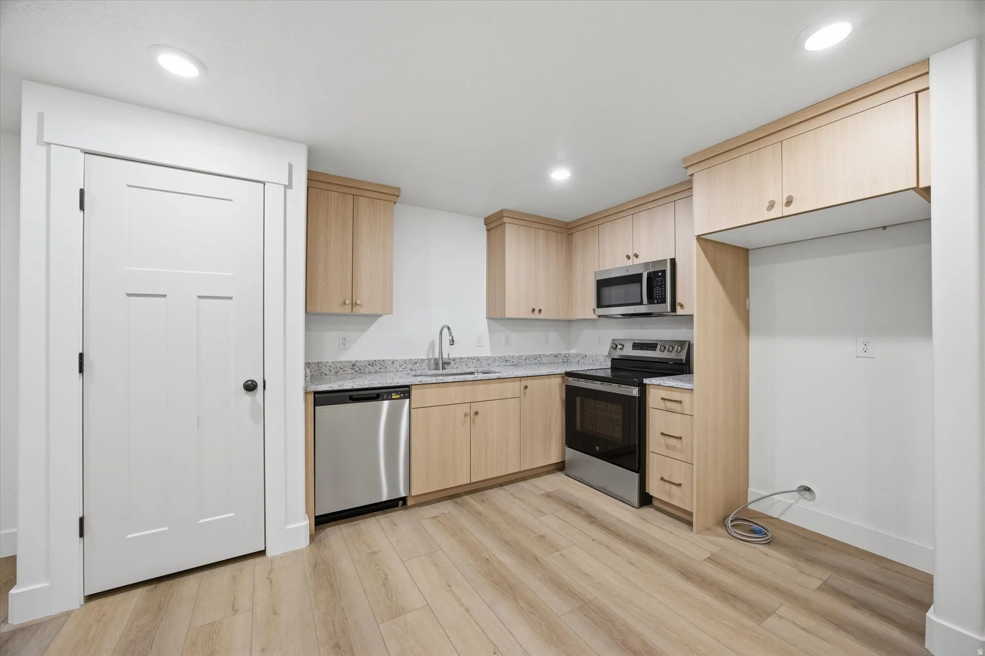 Kitchen featuring stainless steel appliances, light wood finish cabinets, light stone counters, light wood finished floors, and recessed lighting