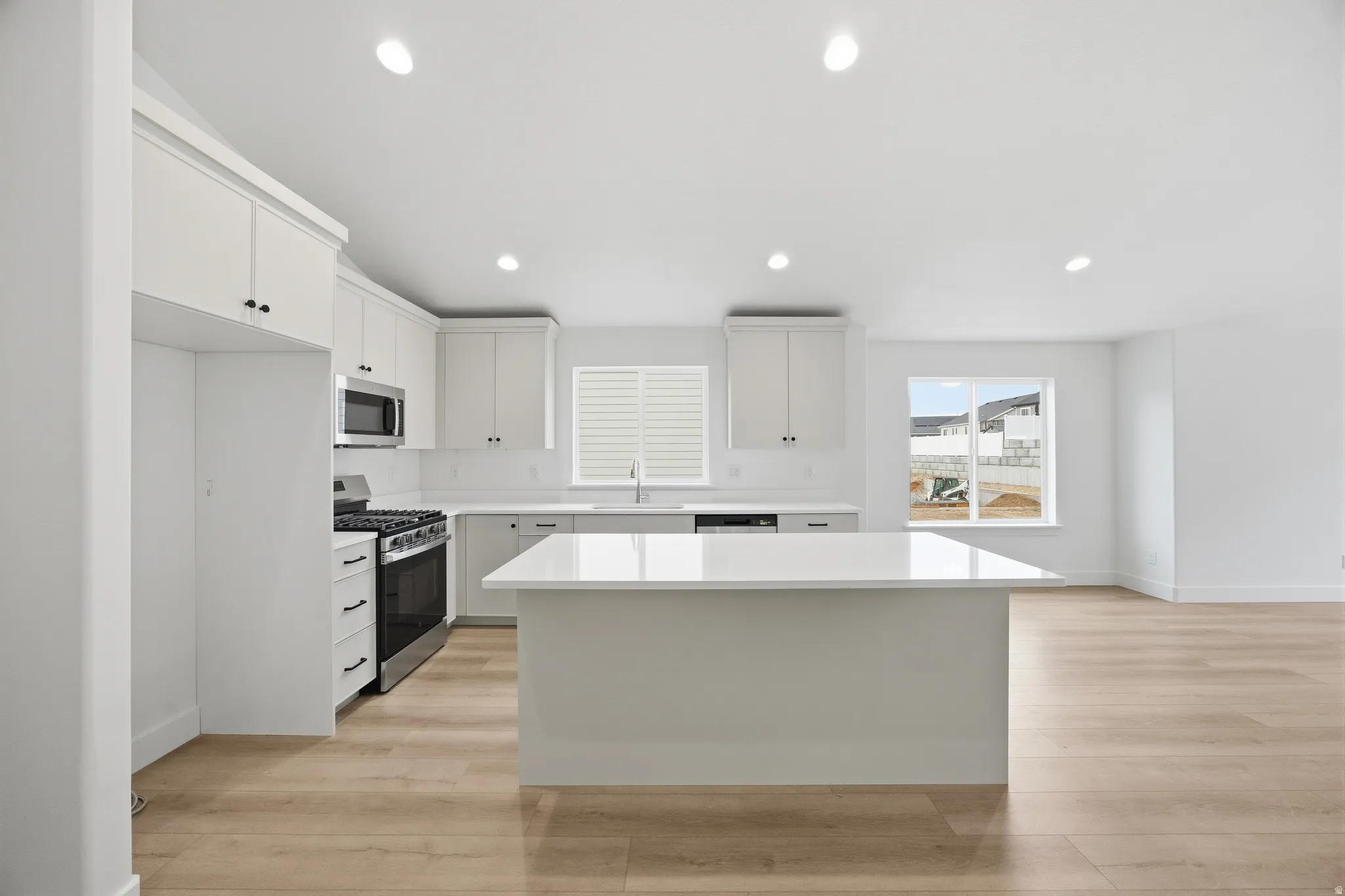 Kitchen featuring stainless steel appliances, light wood-type flooring, a kitchen island, recessed lighting, and white cabinets