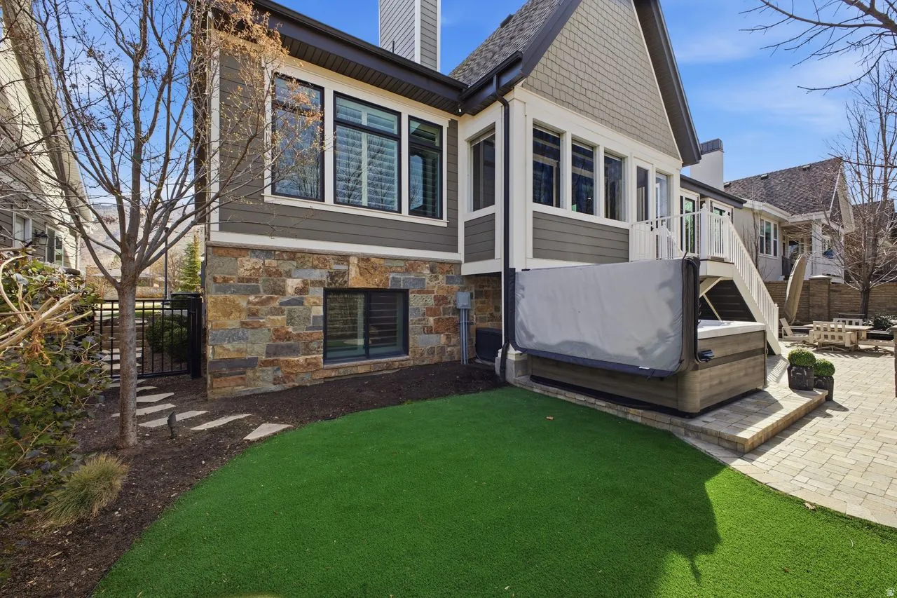 Back of property with a hot tub, a chimney, a patio, stone siding, and a wooden deck