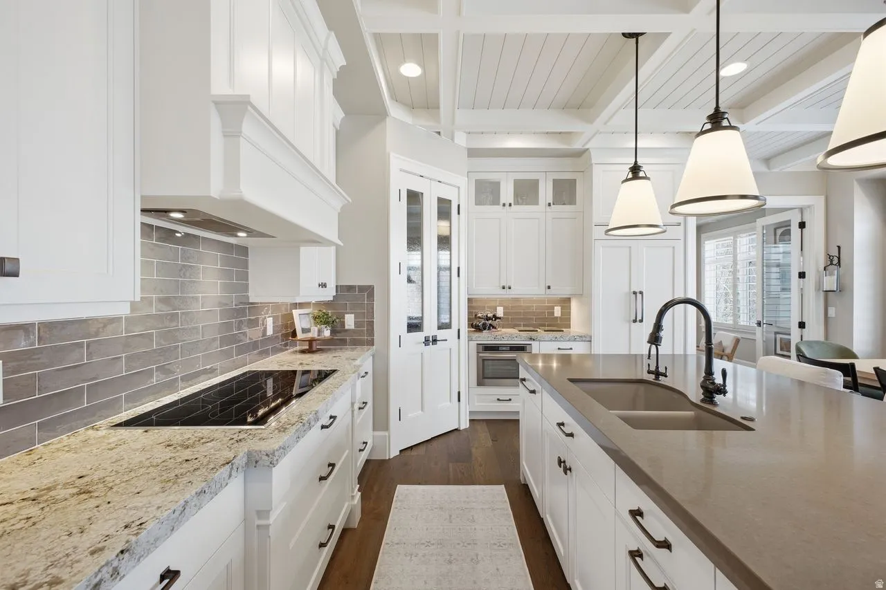 Kitchen with white cabinets, light stone counters, dark wood-style floors, black electric stovetop, and pendant lighting