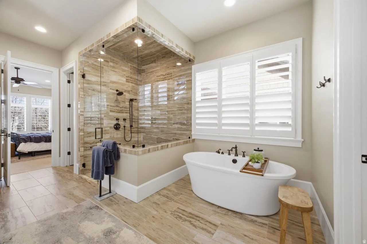 Primary bathroom featuring a shower stall, ensuite bath, a soaking tub, and a ceiling fan