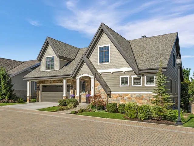 Gabled residence featuring stone and siding exterior, a paver driveway, and an integrated garage