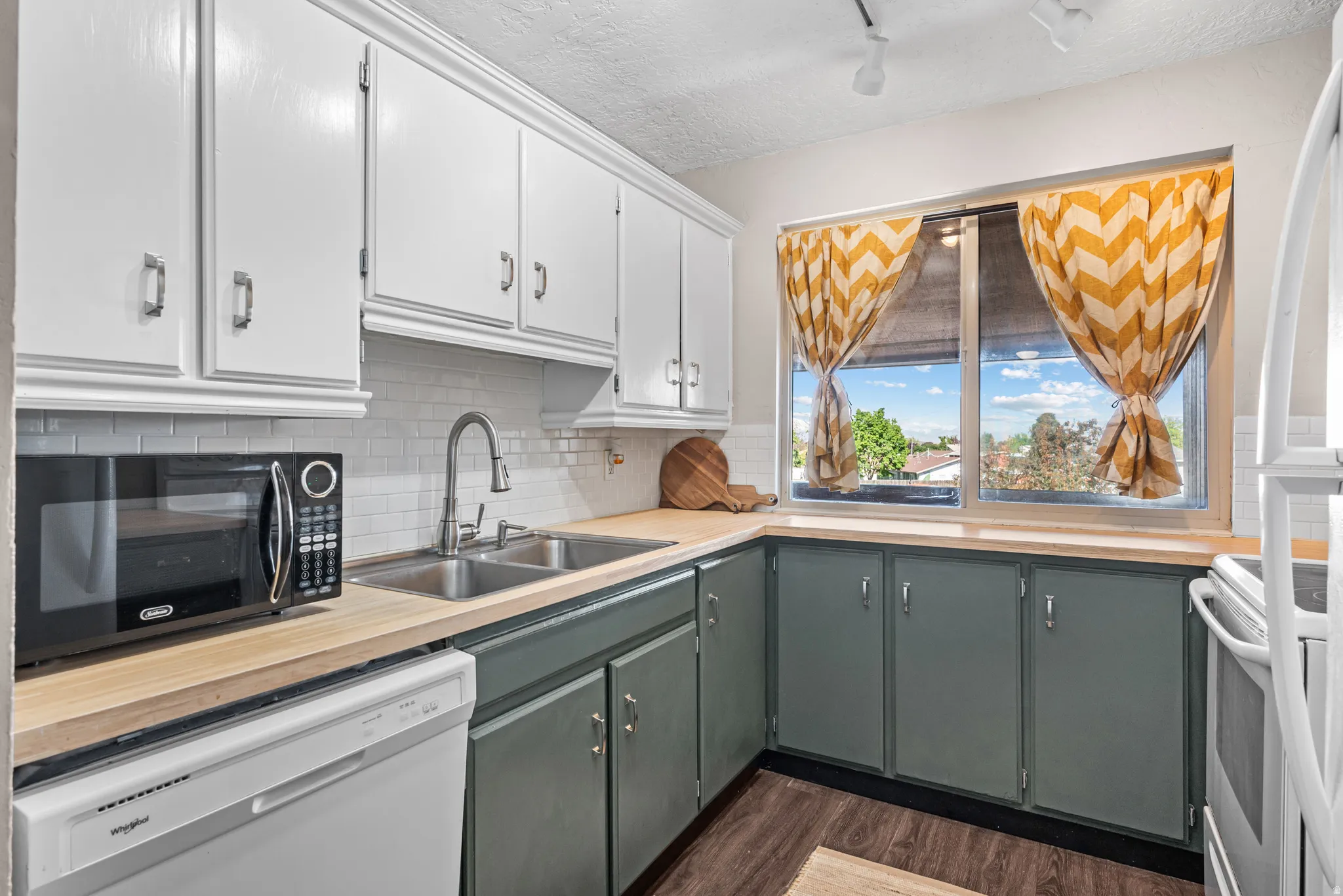 Two tone kitchen featuring a textured ceiling, two tone cabinets, white appliances, dark wood-style floors, and tasteful backsplash