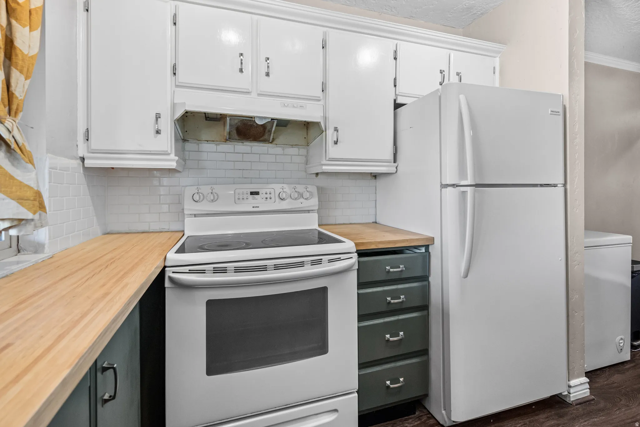 Kitchen featuring white appliances, tasteful backsplash, butcher block countertops, dark wood-style floors, and dual tone cabinets