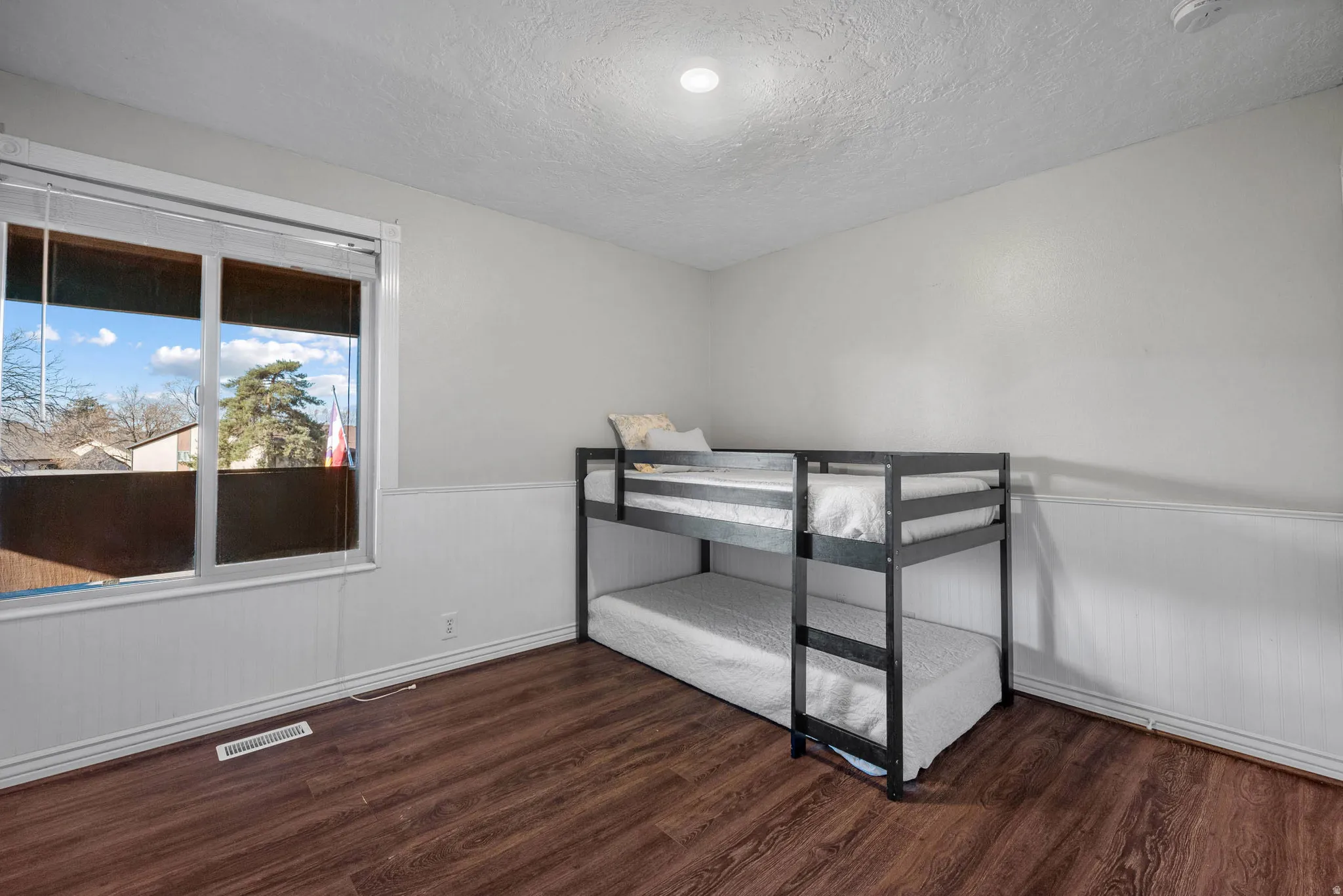 Unfurnished bedroom with a wainscoted wall, dark wood finished floors, and a textured ceiling