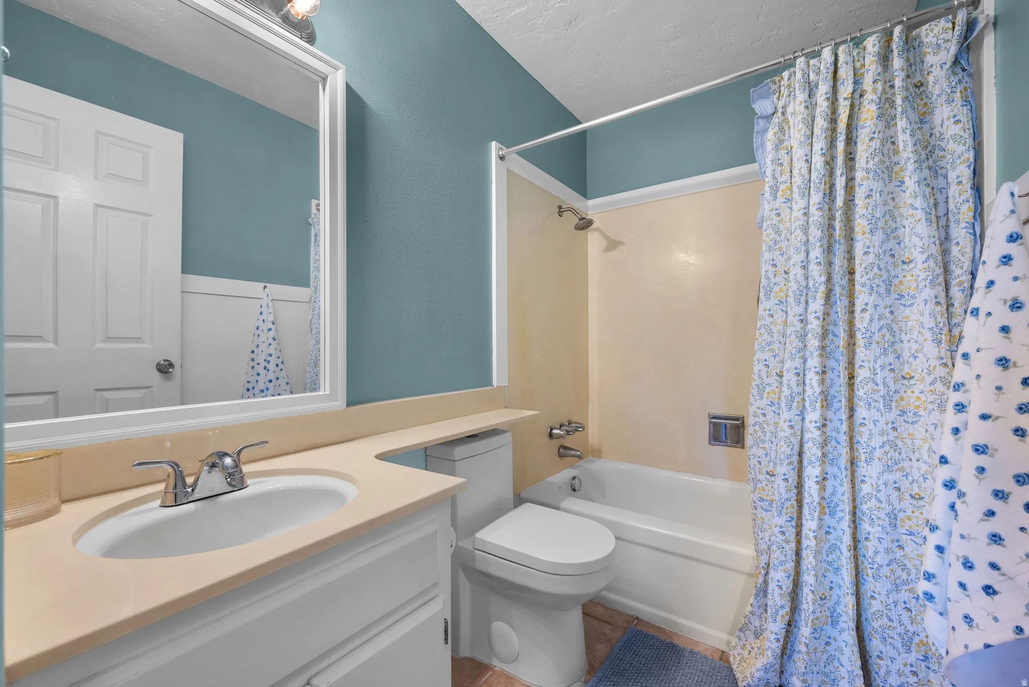 Full bathroom featuring a textured ceiling, vanity, and shower / bath combination with curtain