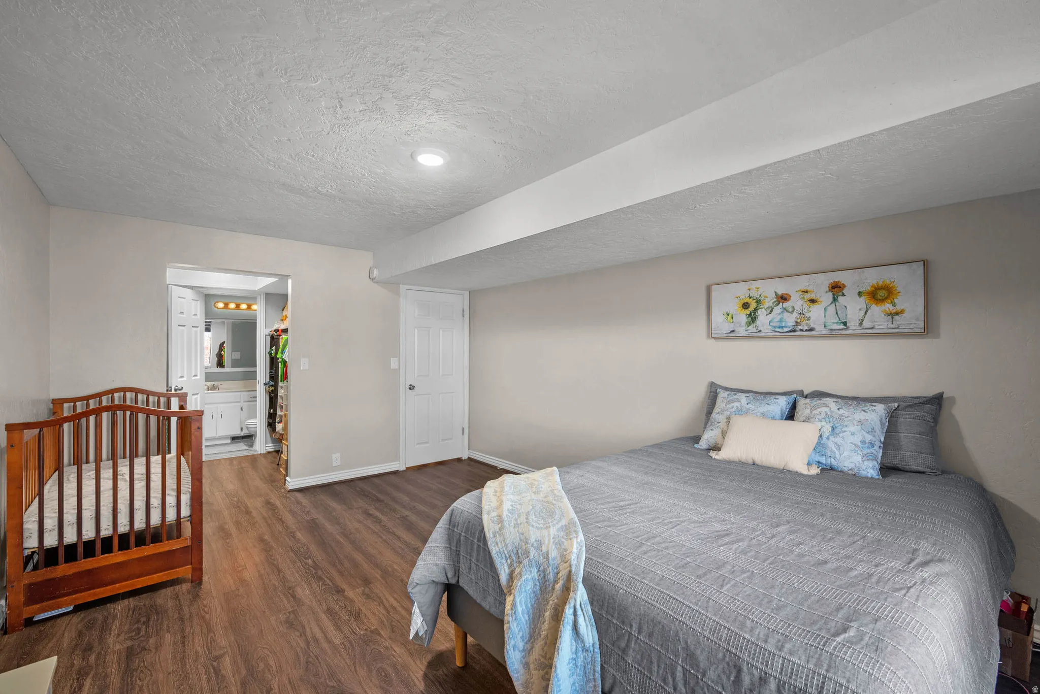 Bedroom featuring dark wood-style flooring, ensuite bath, and a textured ceiling