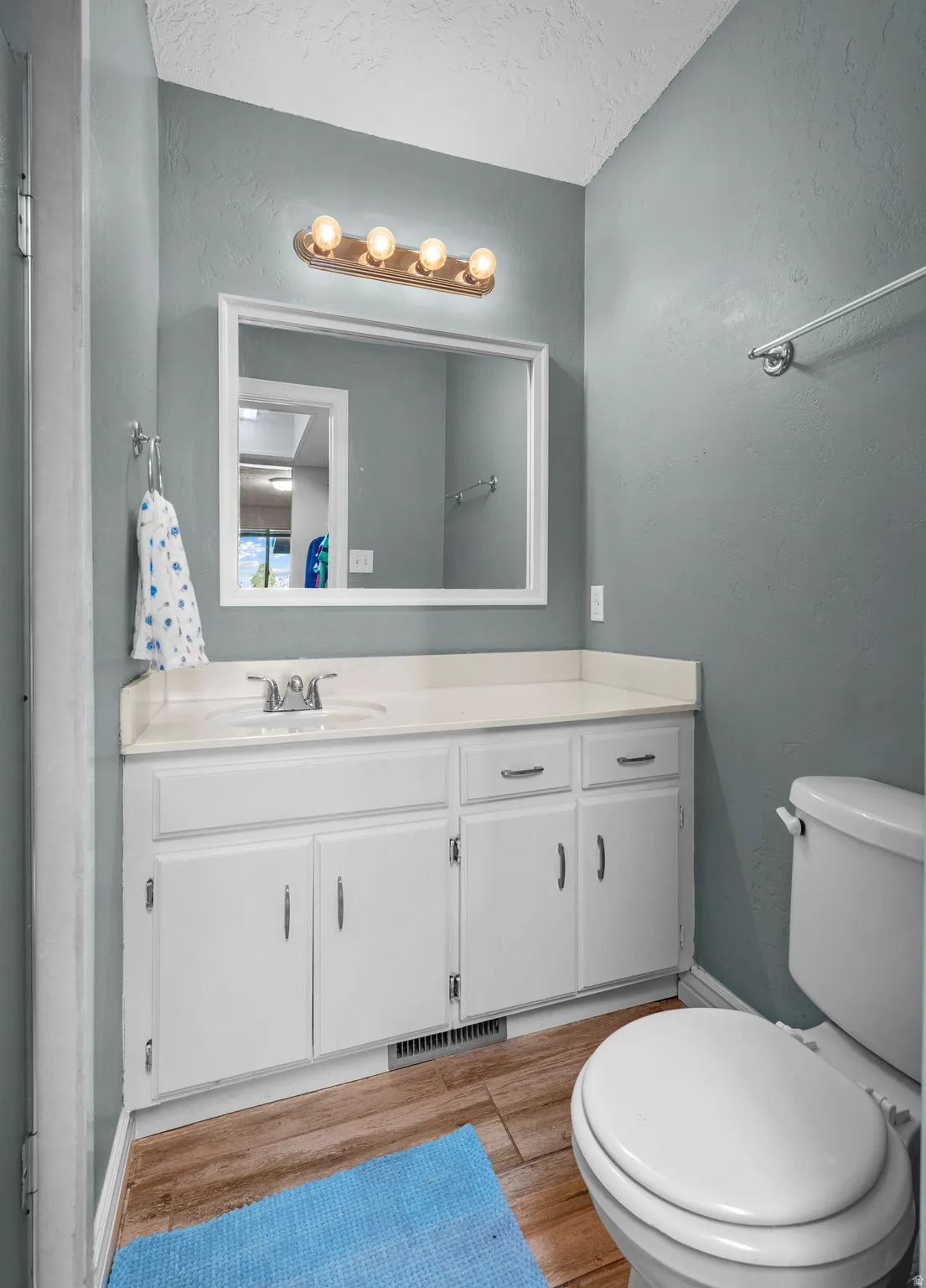 Bathroom with vanity, a textured wall, light wood-style flooring, and a textured ceiling
