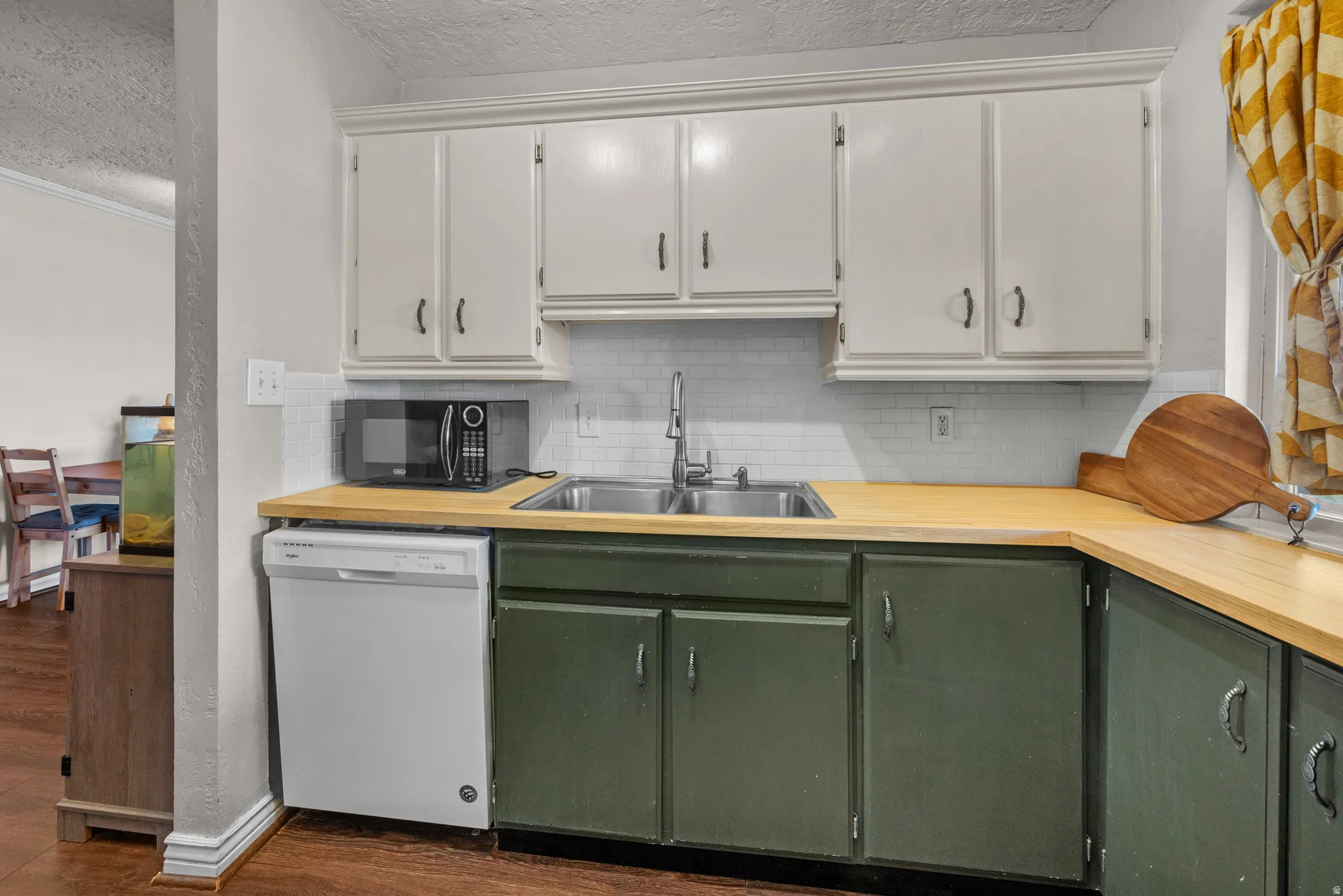 Two tone kitchen featuring two tone cabinetry, dishwasher, a textured ceiling, dark wood-style floors, and decorative backsplash