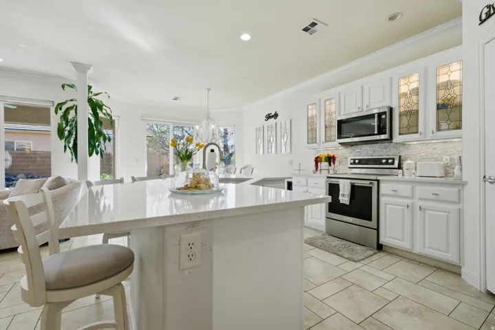 Kitchen with white cabinetry, stainless steel appliances, a kitchen island with sink, ornamental molding, and decorative backsplash