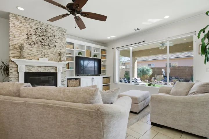 Living area with ceiling fan, a fireplace, light tile patterned floors, built in shelves, and ornamental molding