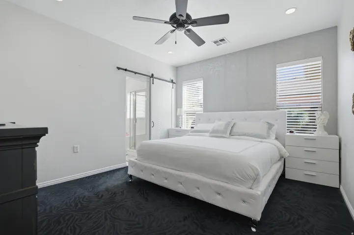Bedroom with dark colored carpet, ceiling fan, a barn door, multiple windows, and recessed lighting