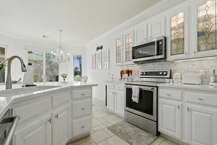 Kitchen featuring stainless steel appliances, white cabinetry, light stone countertops, glass insert cabinets, and ornamental molding